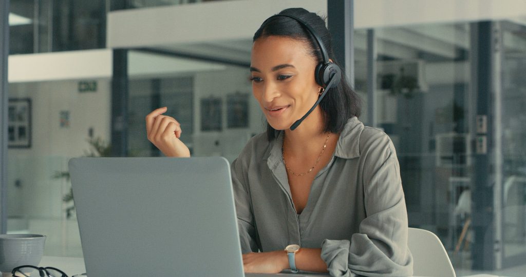 A woman wearing a headset, sitting at a desk with a laptop.